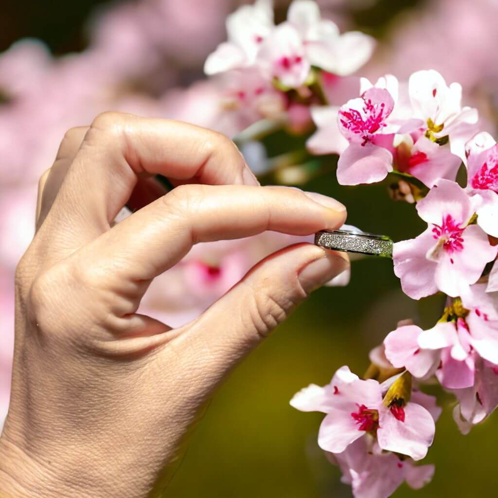 Woman&#39;s hand holding a silver fidgeting ring between index and thumb on a blurred cherry blossom background
