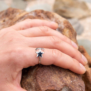 Woman's hand on an orange rock wearing a moon and star spinning ring on her index finger