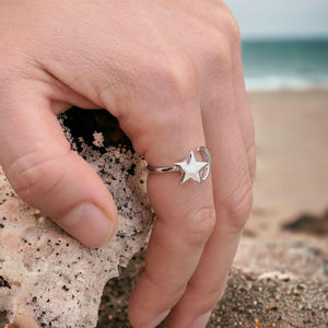 Woman's hand on a rock wearing moon and star ring for fidgeting with a beach background