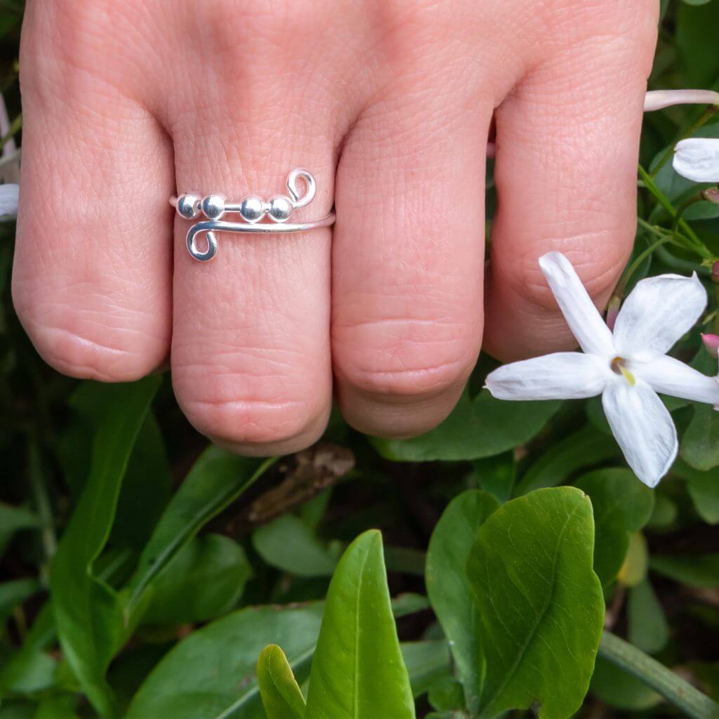 Woman&#39;s hand wearing a sterling silver ring with beads next to white flowers