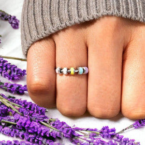 Woman's hand wearing a fidget ring with enamel beads next to lavender flowers