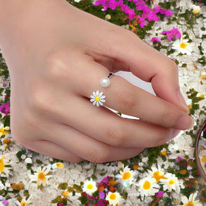 Woman's hand wearing a flower pearl ring adjustable on index finger on multicolored flowers background