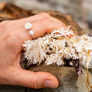 Woman's hand wearing a flower pearl ring adjustable on index finger on a rock next to seaweed