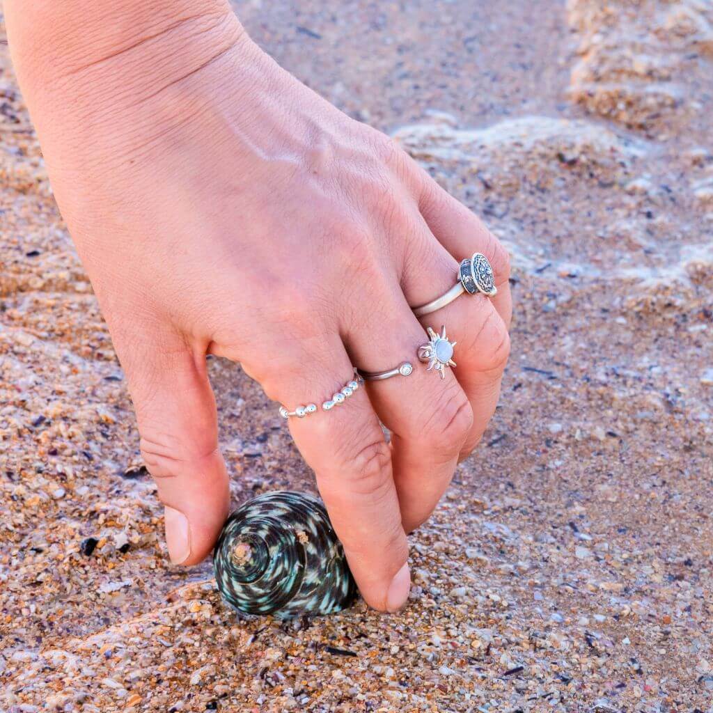 Woman&#39;s hand wearing 3 stress rings holding a shell on sand background