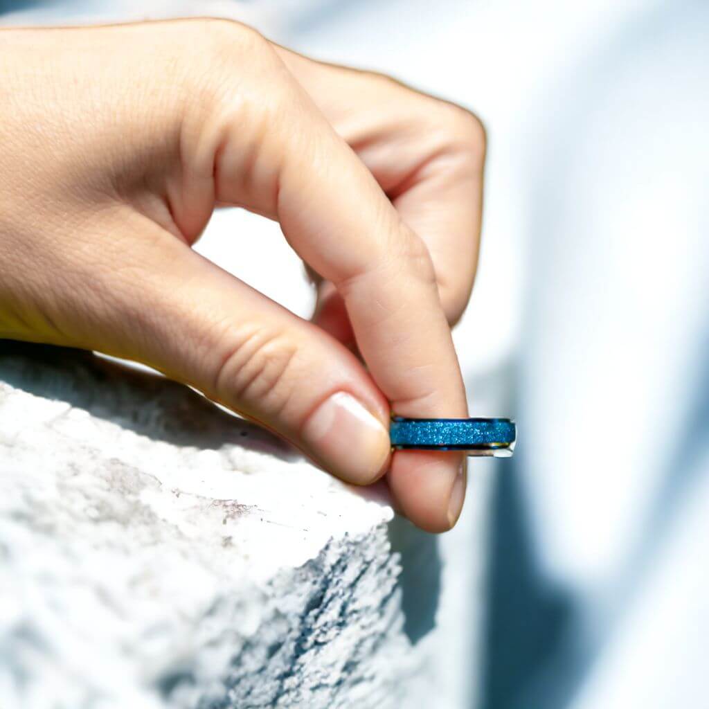 Woman's hand on a white stone holding a blue fidgeting ring between index and thumb on blurred white background