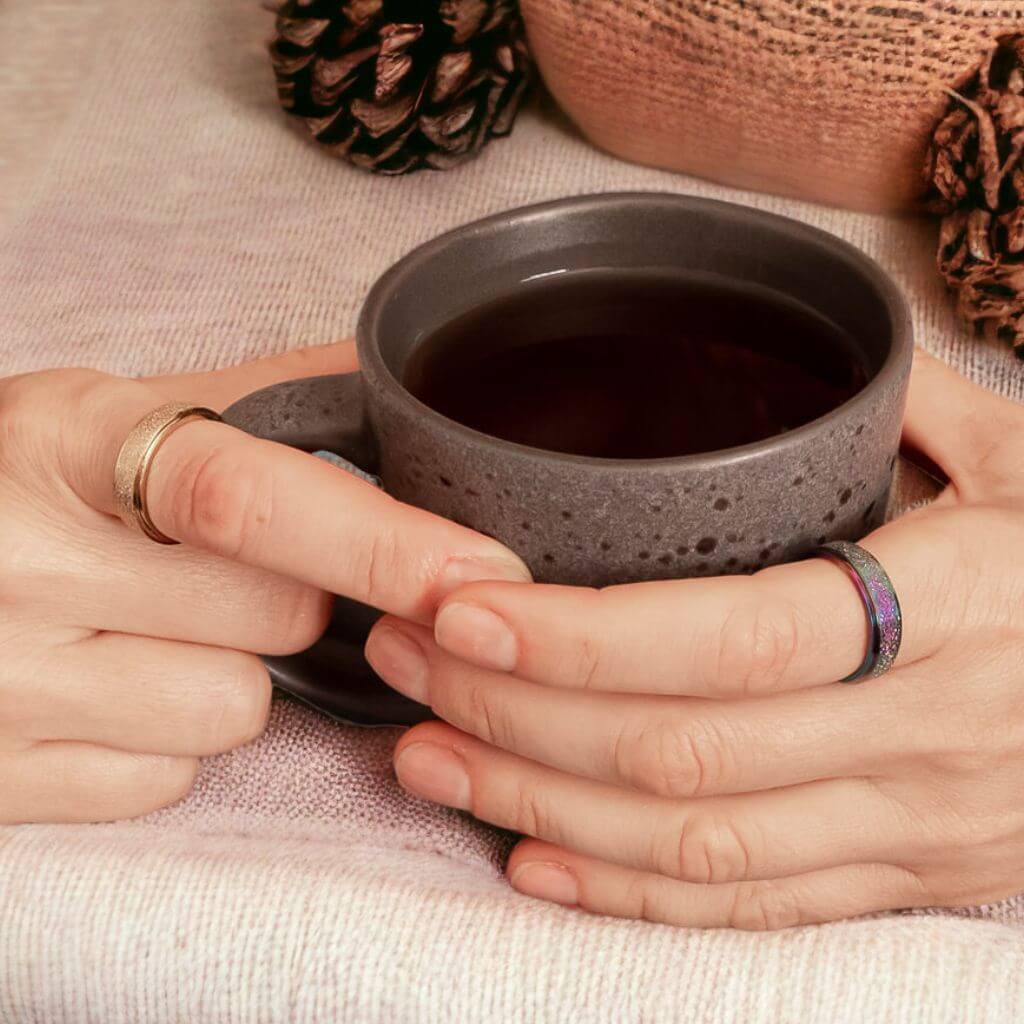 Woman&#39;s hands holding a tea mug wearing gold and rainbow fidget rings on a cozy earthly background