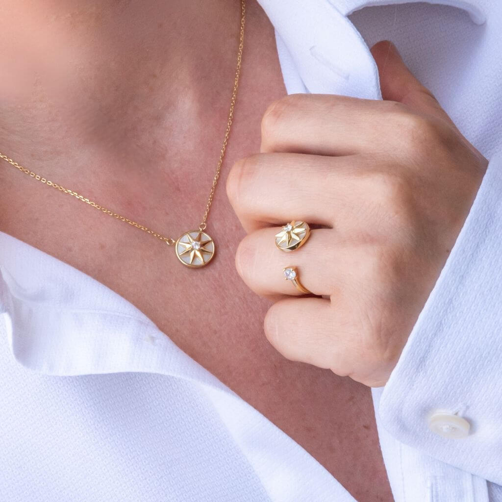 Gold jewelry set featuring a round starburst pendant necklace and matching starburst ring, shown on a model wearing a white collared shirt.