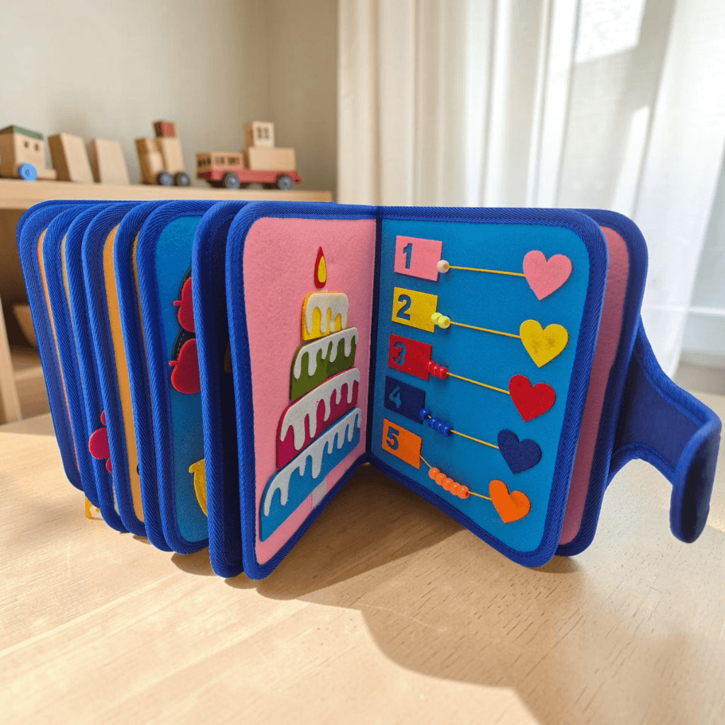 26-page felt busy book open on wooden table showing birthday cake page and number bead counting activity with heart shapes