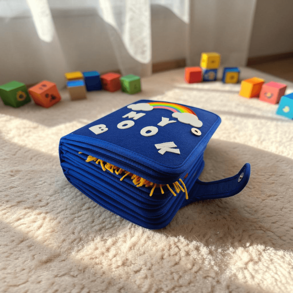 Closed felt busy book with blue My Book rainbow cover and carry handle, surrounded by colourful wooden blocks