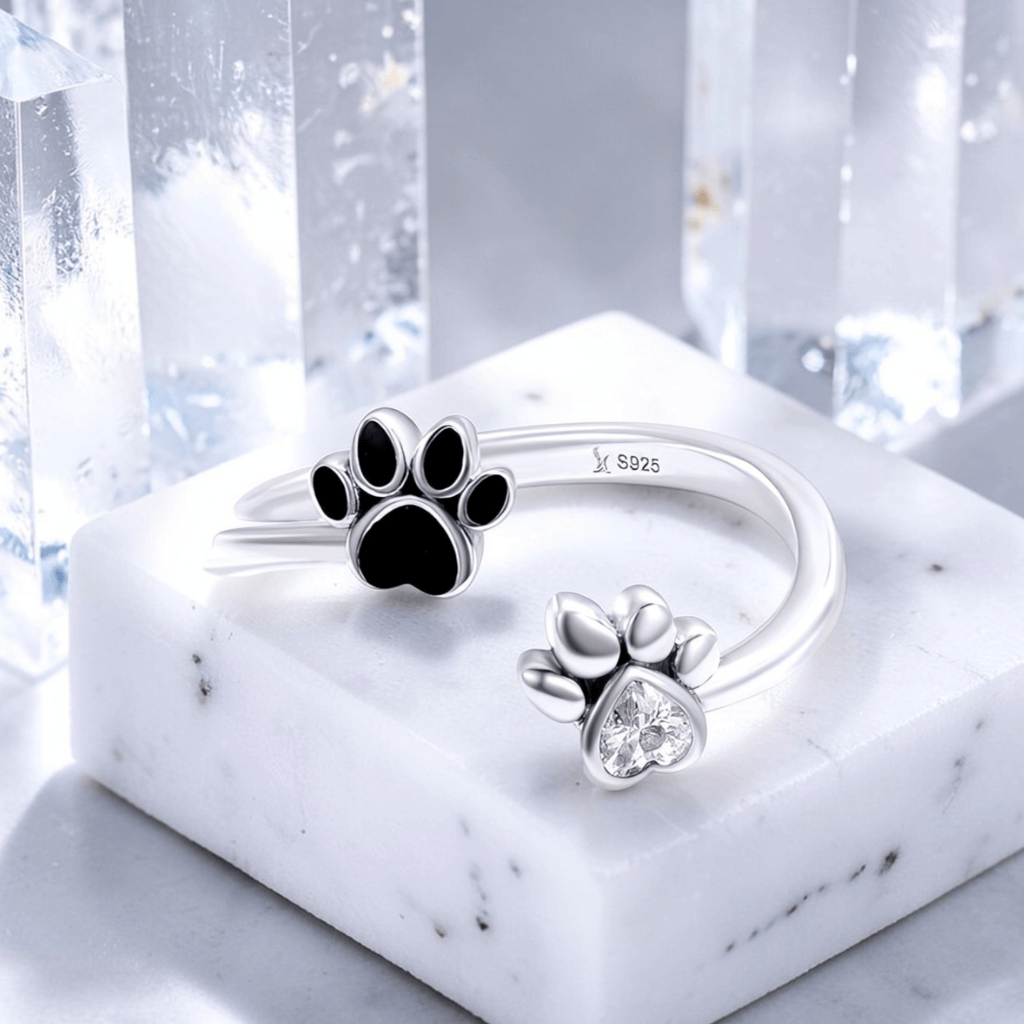 Silver paw print ring with black and clear stones on a marble base with a snowy background