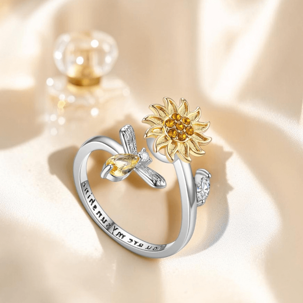 Two-tone sunflower bee fidget ring showing you are my sunshine engraving inside band on cream silk with perfume bottle