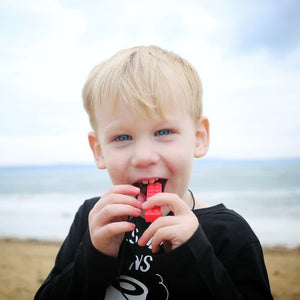 Caucasian toddler chewing on a red Ark's brick stick textured sensory chew necklace