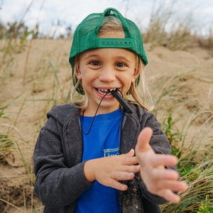 Toddler wearing a baseball cap smiling while chewing on Ark's krypto bite sensory necklace