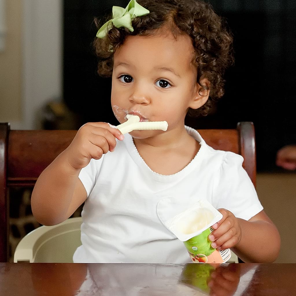 Toddler girl eating yogurt with Ark's Y shaped textured sensory chewing tool