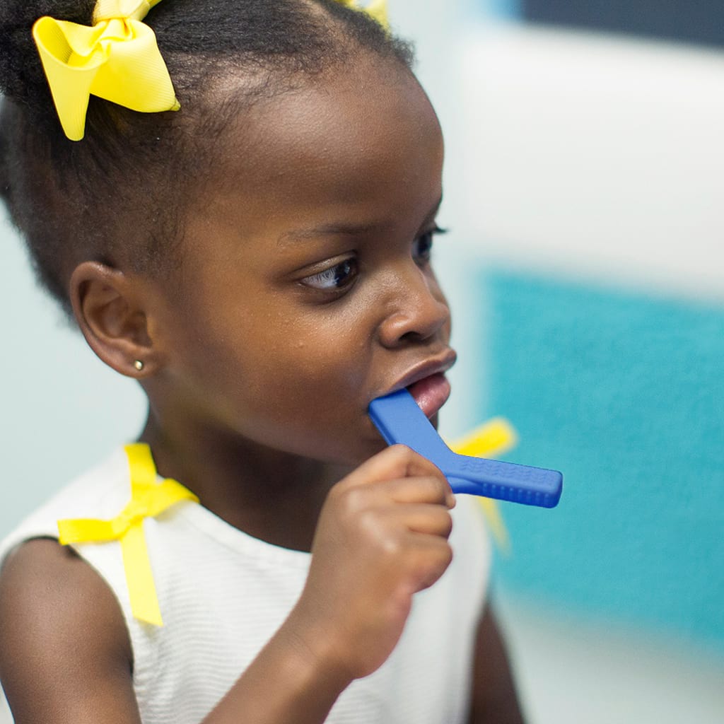 Afro american toddler girl chewing on Ark&#39;s Y shaped sensory chew toy in royal blue YC100XXTRoyalAW