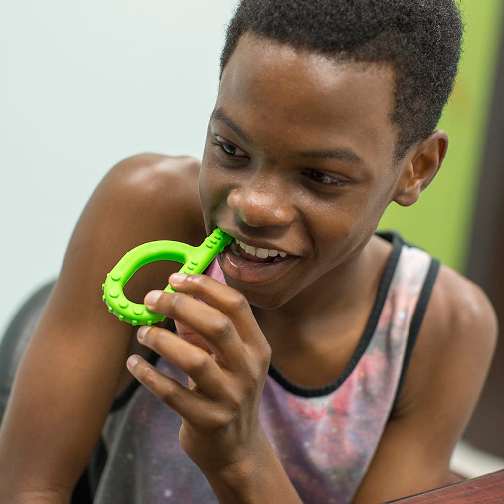 Afro american teenager boy chewing on Ark's textured grabber sensory toy to manage anxiety and stress