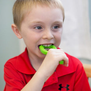 Caucasian boy chewing on Ark's textured grabber silicone chew toy in lime green medium toughness
