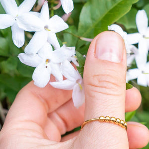 Finger wearing a gold beaded adjustable ring next to white flowers