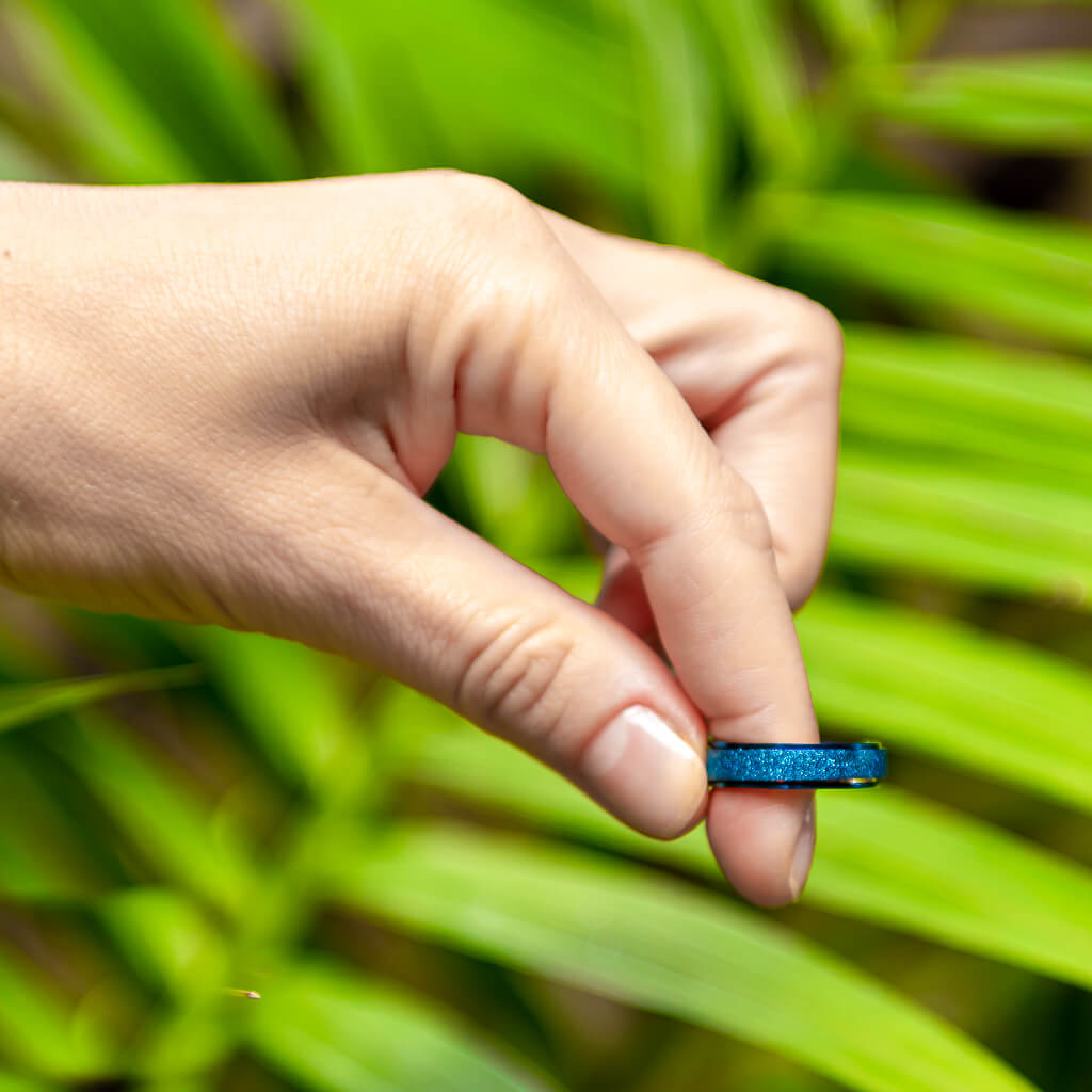 Woman&#39;s hand holding a blue sparkling spinner ring in Australia on palm leaf background